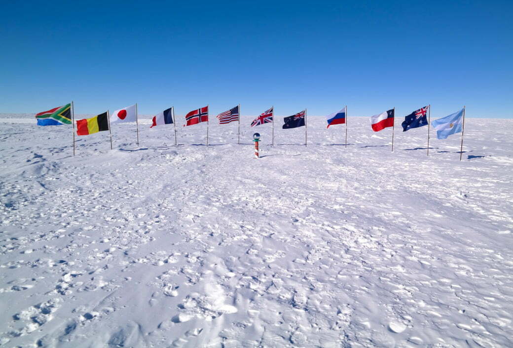 twelve flags planted in the white sastrugi snow surrounding the ceremonial south pole marker which t20 GGR090 Antarctica's first flag hopes to give the continent a voice in the climate crisis